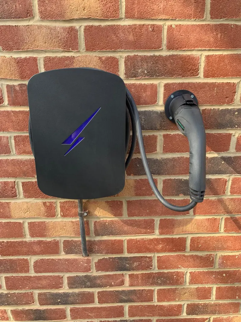 Black EV charger with a purple light and tethered cable, fixed to red brick