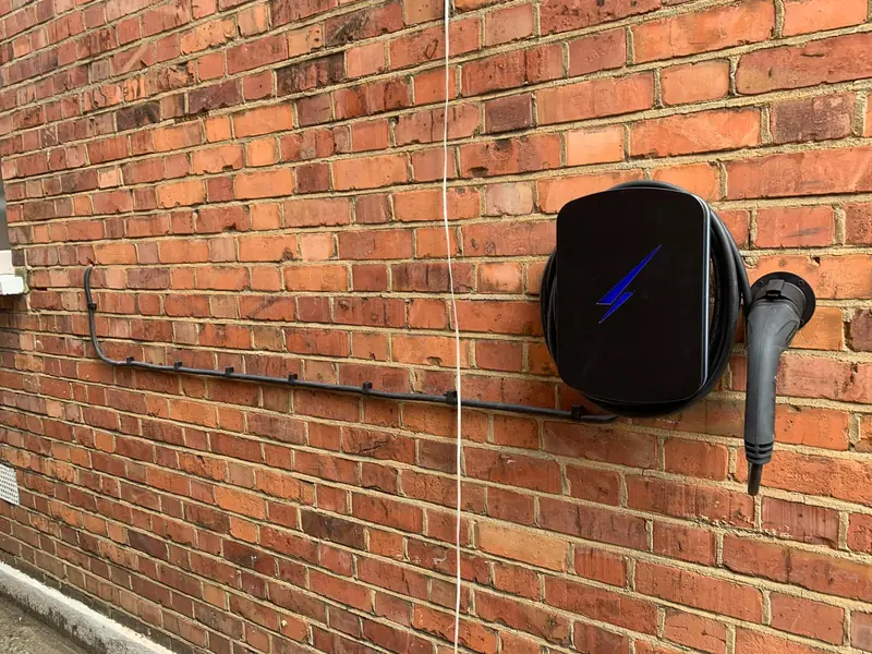 Black EV charger on a long brick wall, its supply cable clipped neatly along the brickwork