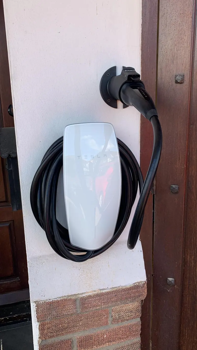 White EV charger with its cable coiled, fixed to a white pillar beside a dark door frame
