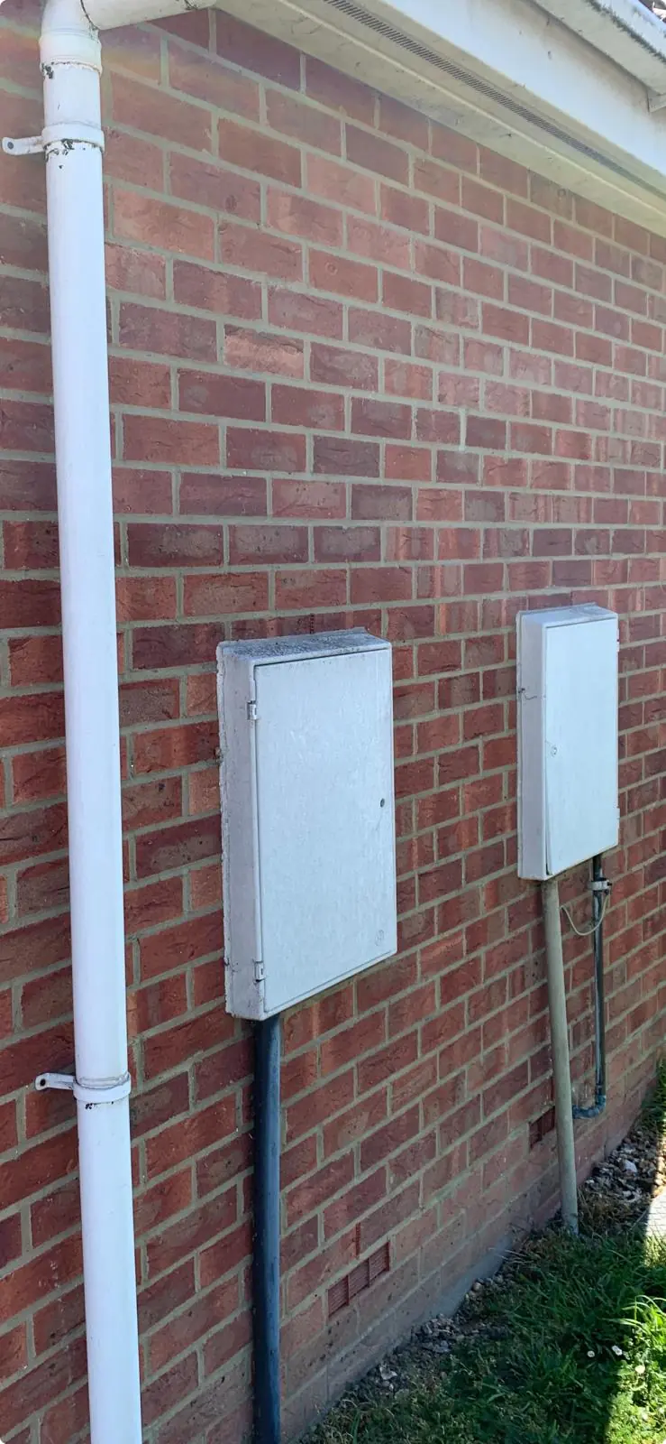 Two external meter cabinets on a brick wall beside a white downpipe