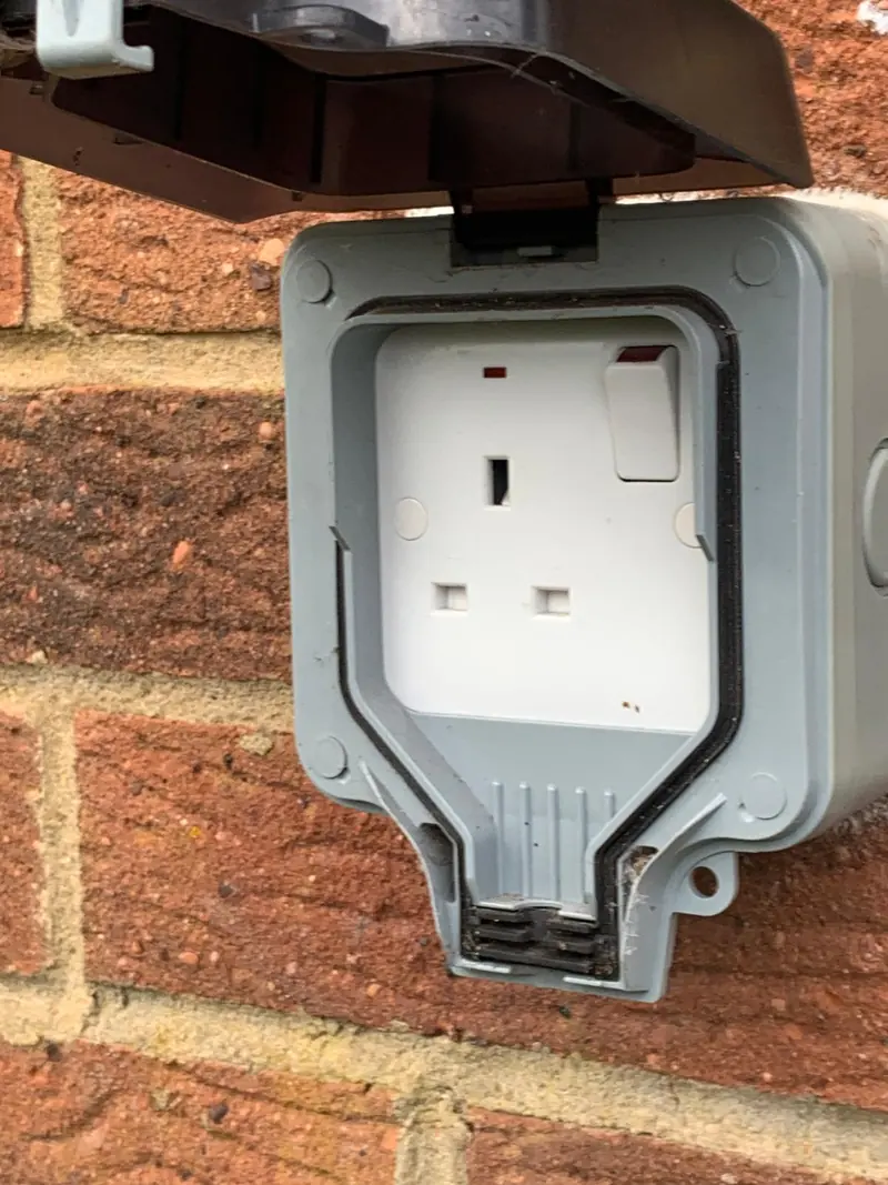 Weatherproof outdoor socket on brick, its hinged lid open