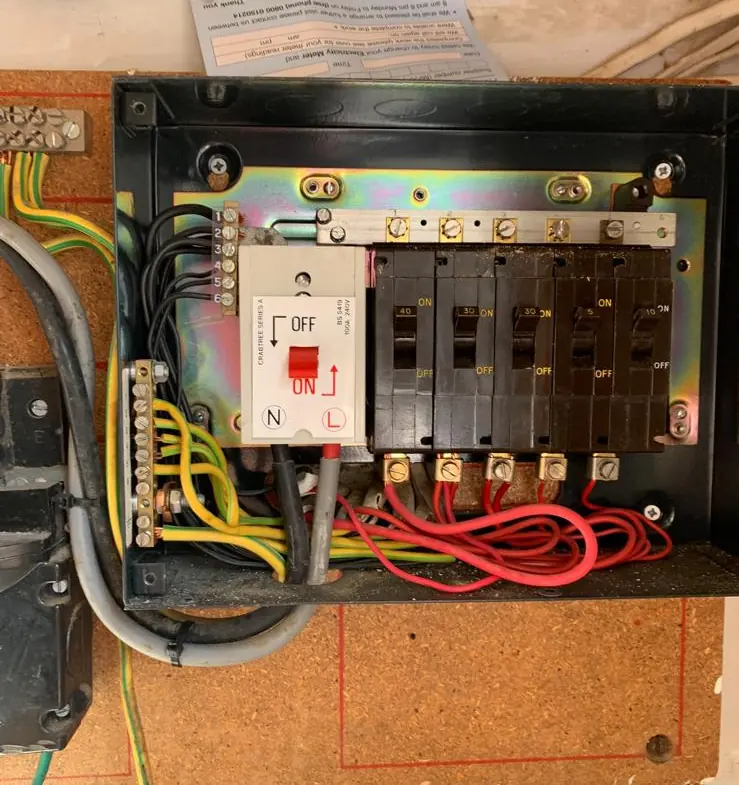 An old fuse board in a black metal enclosure: a main switch and a row of circuit breakers, with no RCD and no surge protection