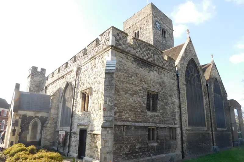 Holy Trinity Church on Dartford High Street: flint walls, battlements and a square tower with a clock, under a blue sky