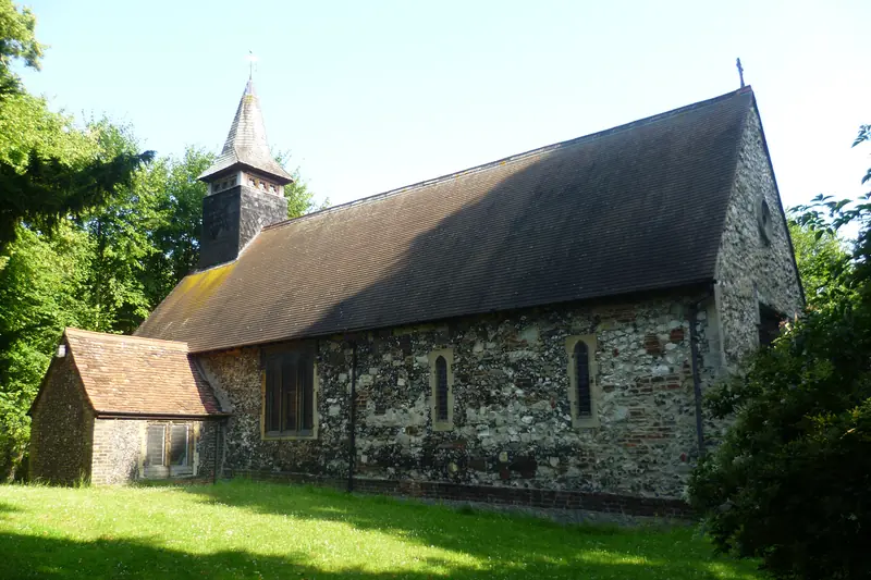 The old church of St Michael at East Wickham: a long tiled roof, flint walls and a small shingled spire among trees